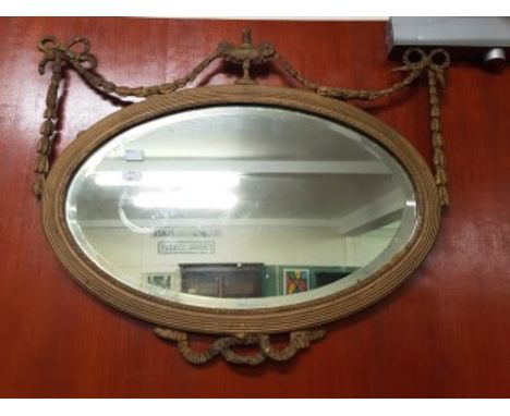 A PAIR OF OVAL GILT ADAMS STYLE WALL MIRRORS, each crested with a two handled urn issuing bell flowers, and two ribbon bows w