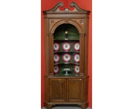 A FINE PINE CORNER CUPBOARD. Eighteenth century and later. Swan-neck and dentil-moulded cornice, above an arched niche enclos