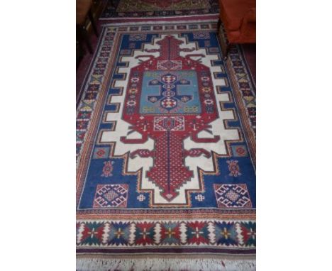 A LARGE TURKISH RUG, with light blue and red medallion, within dark blue stepped spandrels, inside an ivory border with styli