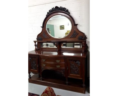 AN EDWARDIAN MAHOGANY BOW FRONTED MIRROR BACK CHIFFONIER OR SIDEBOARD. Top crested with a shell over an oval mirror panel and