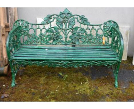 A HEAVY GREEN PAINTED CAST-IRON GARDEN BENCH. The back with scrolling oak branches and ivy, above a slatted seat and conformi