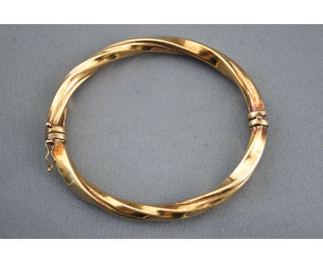 A yellow metal hollow twisted bangle. Hinged clasp with figure of eight safety catch. Stamped 375 for 9ct gold. 12.6 grams