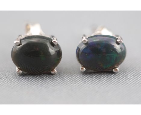 A white metal pair of single stone stud earrings. Each set with an oval cabochon cut blue/green Ethiopian opal. Post and scro