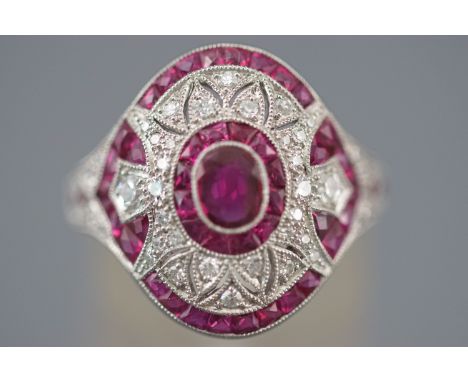 A white metal cluster ring set with an oval faceted cut ruby measuring approximately 5.00mm x 4.00mm. Further set with calibr