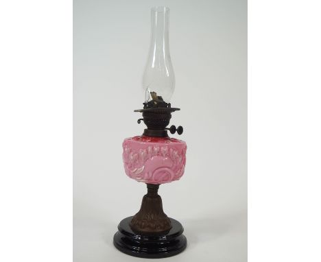 An early 20th century oil lamp with moulded pink glass reservoir, picked out in enamels, overall 60cm high