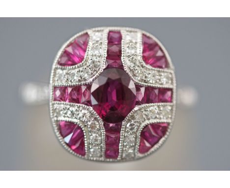 A white metal panel cluster ring set with an oval faceted cut ruby measuring approximately 6.00mm x 5.00mm. Further set with 