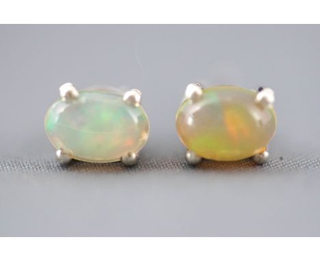 A white metal pair of single stone stud earrings. Each set with an oval cabochon cut Ethiopian opal. Post and scroll fittings