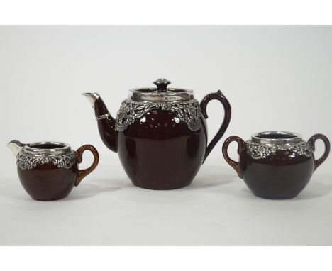 An early 20th century brown glazed pottery tea service with silver mounts, the teapot Birmingham 1906, with the spout hallmar