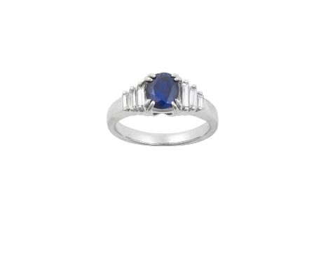 A Sapphire and Diamond Ringthe oval cut sapphire in a white double claw setting, flanked by trios of graduated baguette cut d