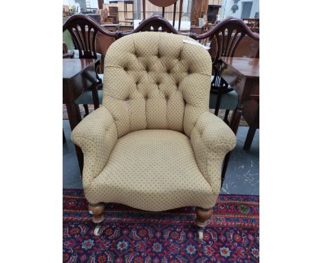 A VICTORIAN BUTTON BACK ARMCHAIR WITH TURNED FRONT LEGS ON CERAMIC CASTERS.
