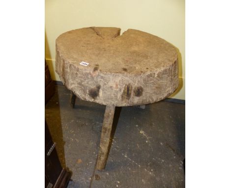 AN ANTIQUE RUSTIC CHOPPING BLOCK ON THREE NATURAL STICK LEGS. 68 x 60 x H.62cms.