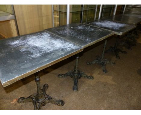 A SET OF FOUR VINTAGE CAFE TABLES WITH CAST IRON BASES AND ZINC WRAPPED PINE TOPS.