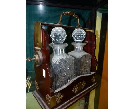 A MAHOGANY TWO BOTTLE TANTALUS, THE BRASS HANDLE AT THE TOP RELEASED BY A BUTTON AND KEY MECHANISM.   W 28cms.