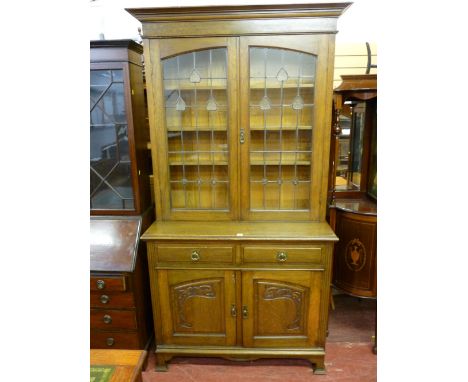 AN OAK ARTS & CRAFTS BOOKCASE TOP SIDEBOARD having an inverted step crown over twin leaded glazed doors with bullseye and hea