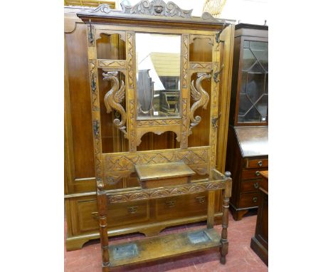 A CARVED OAK MIRRORED HALLSTAND with mask and mythical beast decoration and six double hooks, central lidded compartment with