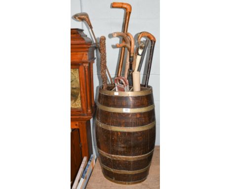 A coopered brass and oak stick stand of barrel form, together with a shooting stick, various walking sticks, an umbrella, and
