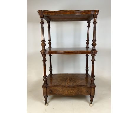 A Victorian serpentine fronted burr walnut three tier inlaid what not with brass and ceramic castors, apron drawer to base.W: