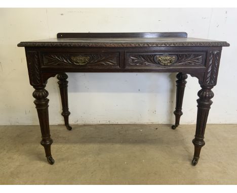 An early 20th century carved oak desk with turned legs and brass and ceramic castors, two drawers with carved fronts and bras