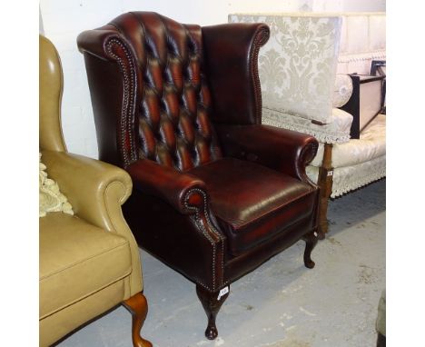 A red leather button-back upholstered wing armchair 