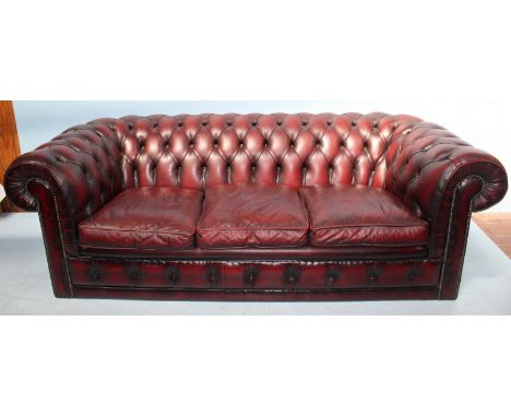 A burgundy leather low back three-seater Chesterfield sofa, with deep button back and sides, scrolled arm rests and brass stu