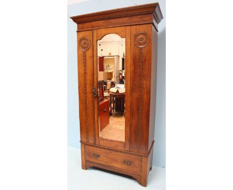 An Edwardian oak wardrobe, the shaped cornice above a single mirrored door opening to reveal hanging and storage space, flank