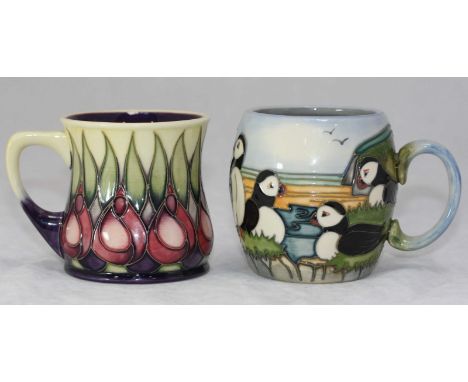 Two Moorcroft ceramic mugs, one being decorated with Puffins, the other April Tulip, dated 1997 and 2002 respectively, both i