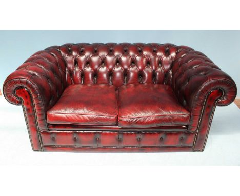 A burgundy leather low back two-seater Chesterfield sofa, with deep button back and sides, scrolled arm rests and brass studd