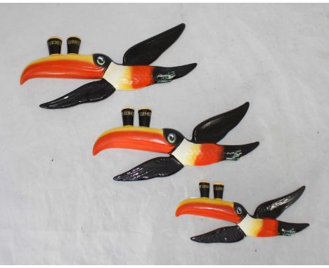 A set of three graduated Carlton Ware ceramic advertising wall plaques modelled as toucans balancing two pints of Guinness on