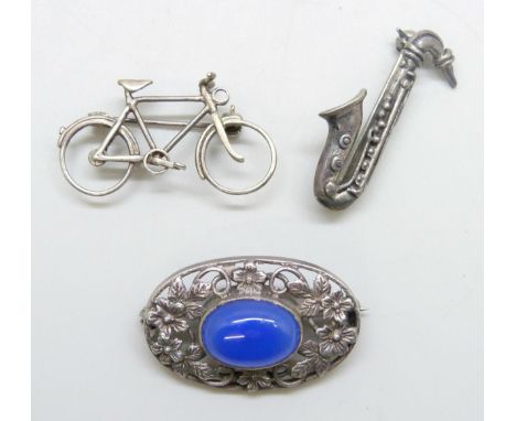 A silver Art Nouveau style brooch set with a blue chalcedony panel, a silver brooch in the form of a saxophone, and a white m
