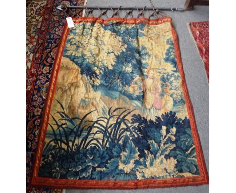 An early 18th century tapestry fragment depicting a milkmaid in rocky landscape with trees, suspended on an iron bracket with