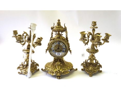 A French gilt brass mantel clock garniture of Louis XVI style, 20th century, the drum case with enamel numerals and ornately 