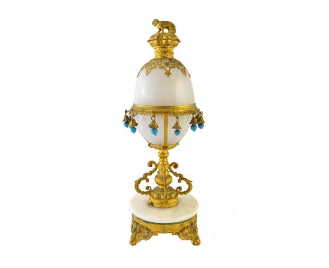 An early 20th century gilt metal and opaque glass mounted scent bottle stand of egg form, with dog finial over a tasselled co