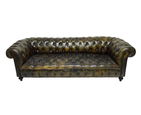 A green leather button upholstered Chesterfield sofa, with studded decoration, on turned ebonised supports, 227cm wide.  Illu