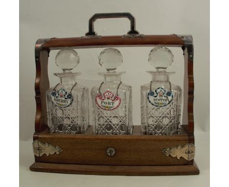 An oak three bottle tantalus, with silver plated mounts, with hinged flap to the front to release the three square glass deca
