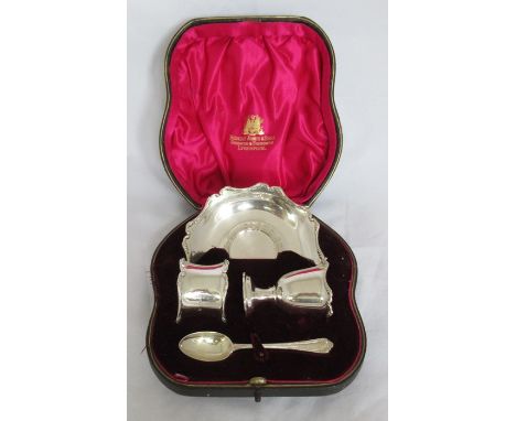 A cased silver christening set, comprising an egg cup, stand, spoon and napkin ring, with scroll edge, London 1909, weight 4o