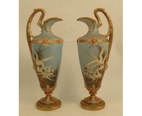 A pair of Royal Worcester ewers, decorated with swans to a powder blue ground, one signed C H C Baldwyn, the other attributed