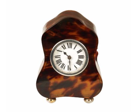 AN EDWARDIAN TORTOISESHELL BOUDOIR CLOCK of serpentine form raised on silver metal squat bun feet, the enamel dial with Roman