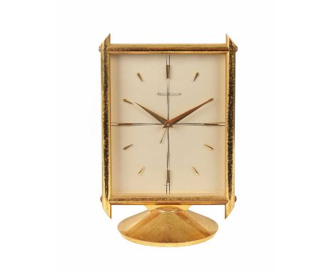 A JAEGER-LECOULTRE GILT BRASS DESK ALARM CLOCK with rectangular moulded frame on circular base enclosing a silvered dial with