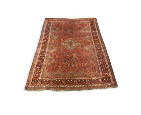 An antique Qashquai red ground carpet, with triple medallions and foliate motifs on a shaped field, multi-bordered,  410 x 34