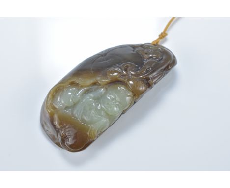 A Chinese celadon and brown jade pendant carved with boy amongst lotus leaves. 7cm length