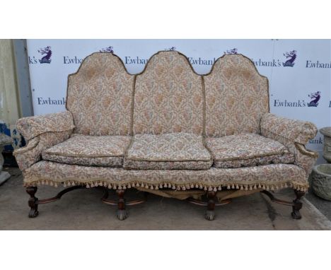 † 1920s three-seater sofa, the arched back over scrolling arms on turned and block legs with scroll feet and shaped cross str