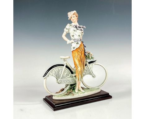 Elegant figure of a woman with her bike. She is dressed in a white floral top and an orange skirt. Florence plaque, impressed