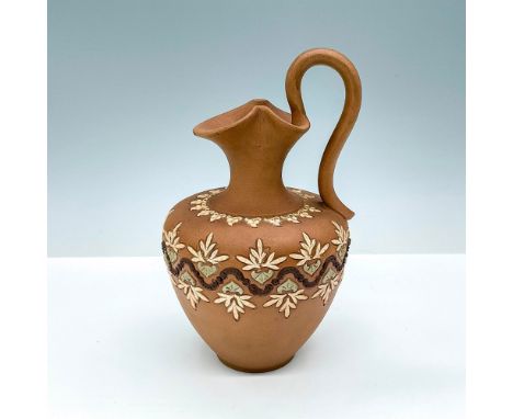 The ewer features a fluted rim and a gracefully arched handle. Its body is adorned with intricate blue and white flowers and 