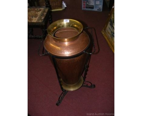 A hammered copper and brass umbrella/stick stand in wrought iron surround
