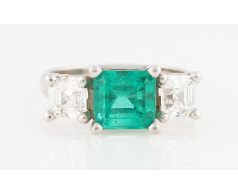 A platinum emerald and diamond three stone ring, the central emerald cut emerald measuring approx. 2.30ct, flanked to either 