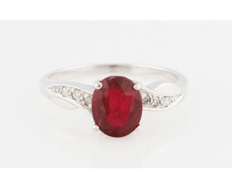 An 18ct white gold ruby and diamond ring, set with a central oval cut ruby, possibly treated, flanked to either side with dia