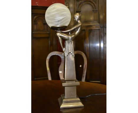 A contemporary table lamp in the form of an Art Deco girl sat on a plinth holding a globe on her knee.