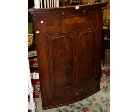 A 19th century bow front mahogany wall mounted corner cupboard, stepped cornice, two raised panel doors over single drawer, b