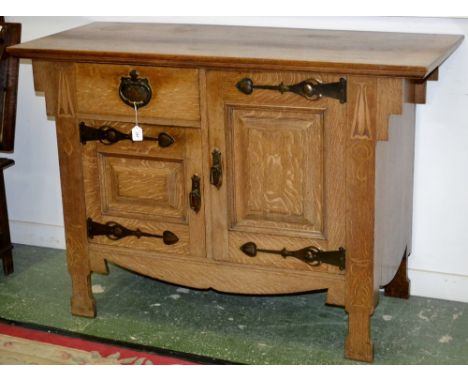 An Arts and Crafts light oak sideboard, oversailing top, an arrangement of two fielded panel cupboards and a short drawer fla
