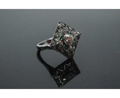 A white gold Art Deco style emerald and diamond ring, the square setting with grain set brilliant cut centre stone surrounded